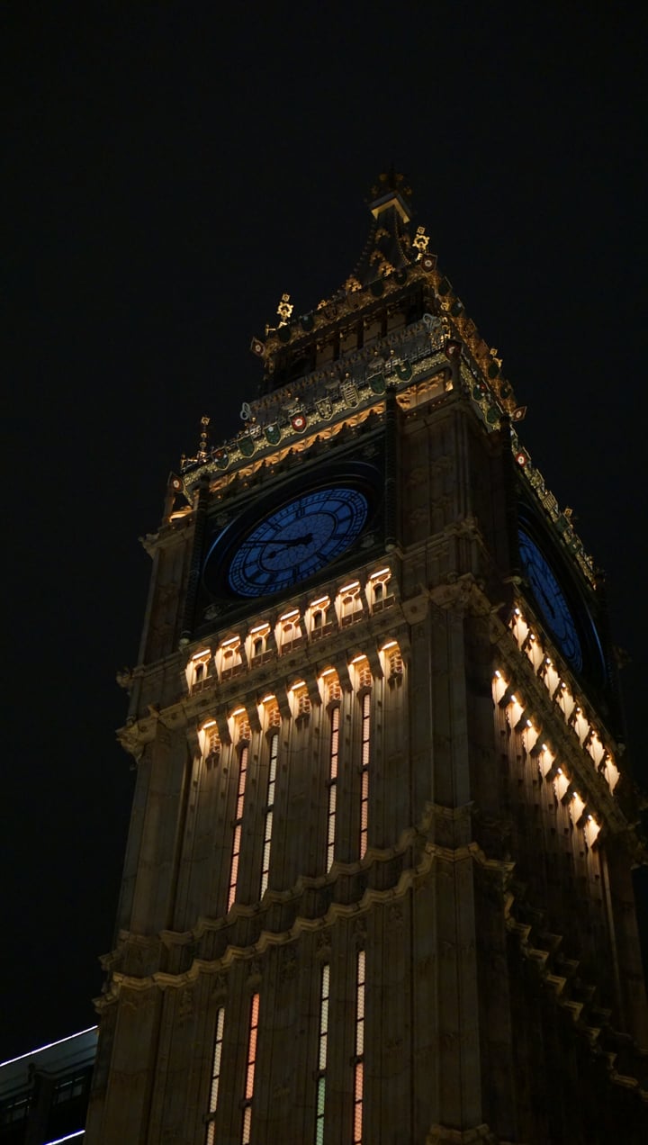 An illuminated clock tower in Macau photographed from below against the night sky