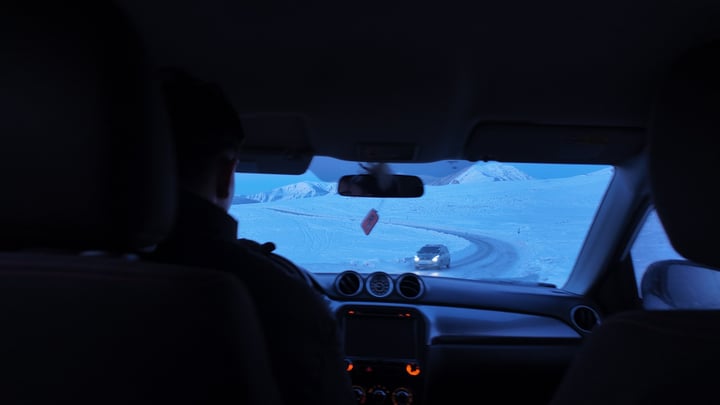 View from the back seat of a car following a road through a snowy landscape