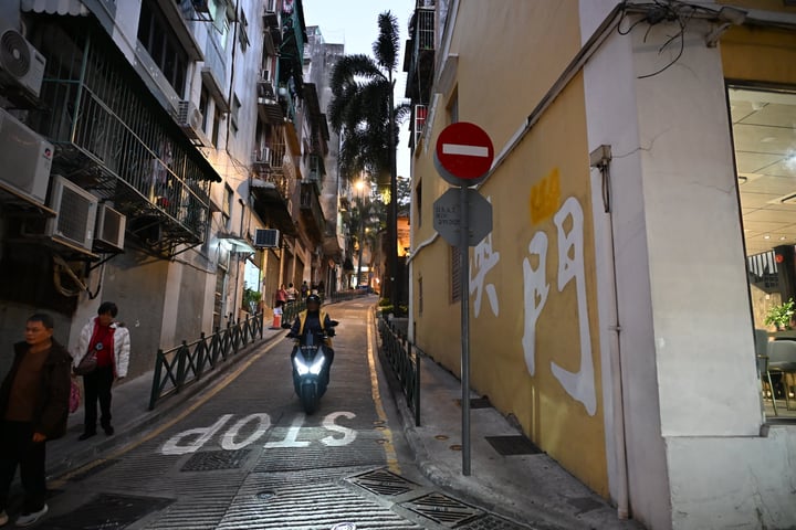 A scooter approaches through a narrow lane between closely spaced buildings