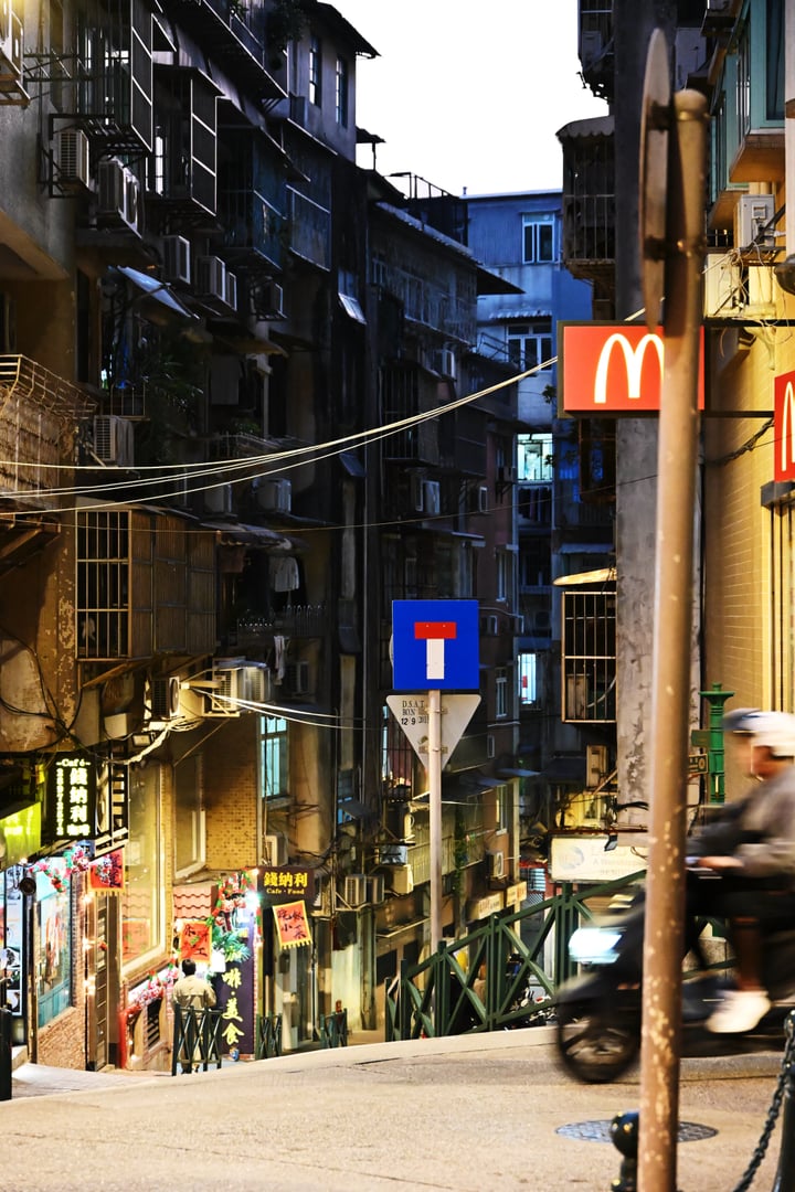 Illuminated shopfronts and signs between tall buildings at dusk