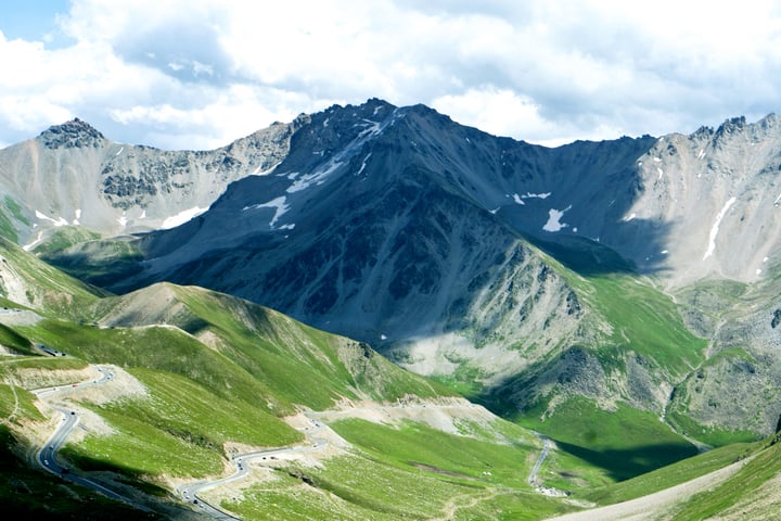 Rocky mountain peaks above bright green slopes and low clouds